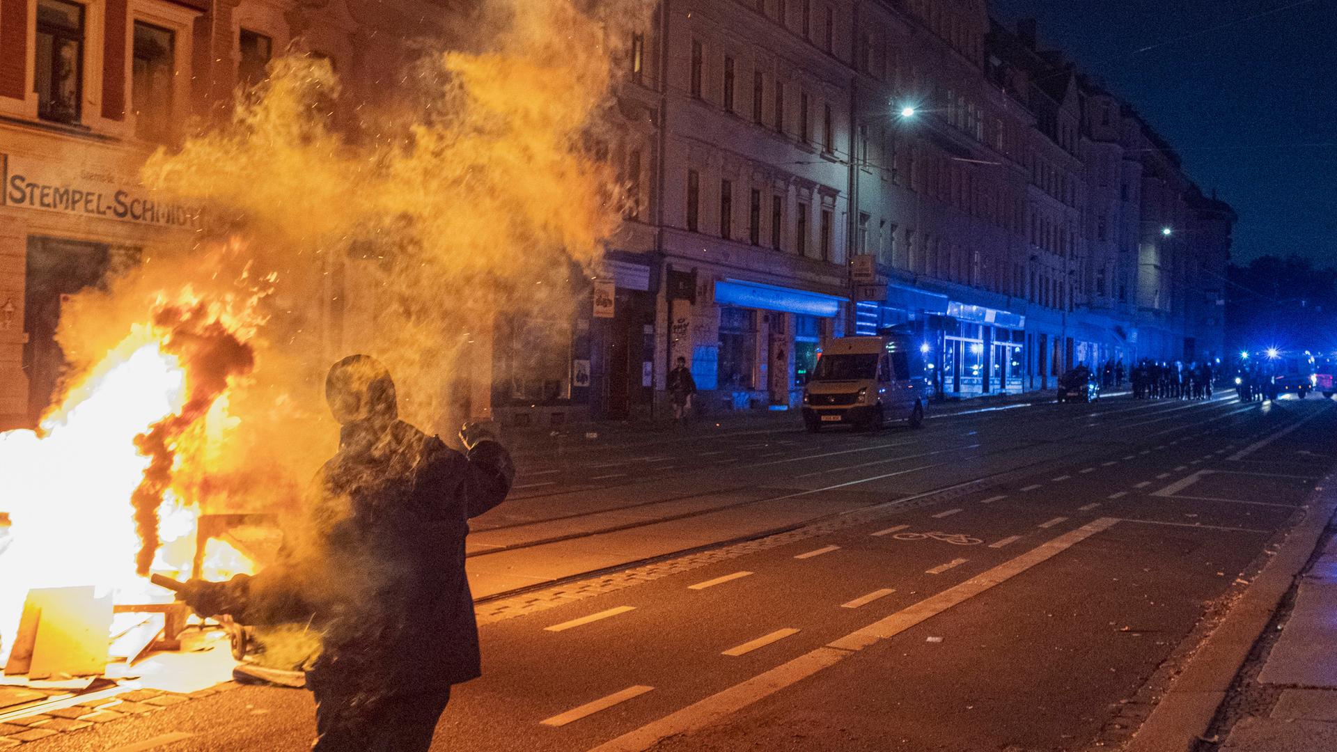 Sachsen, Leipzig: Ein maskerter Demonstrant steht mit brennender Pyrotechnik in der Hand auf einer Straße nach dem Urteil gegen die linksextremistische Grupp Antifa-Ost.