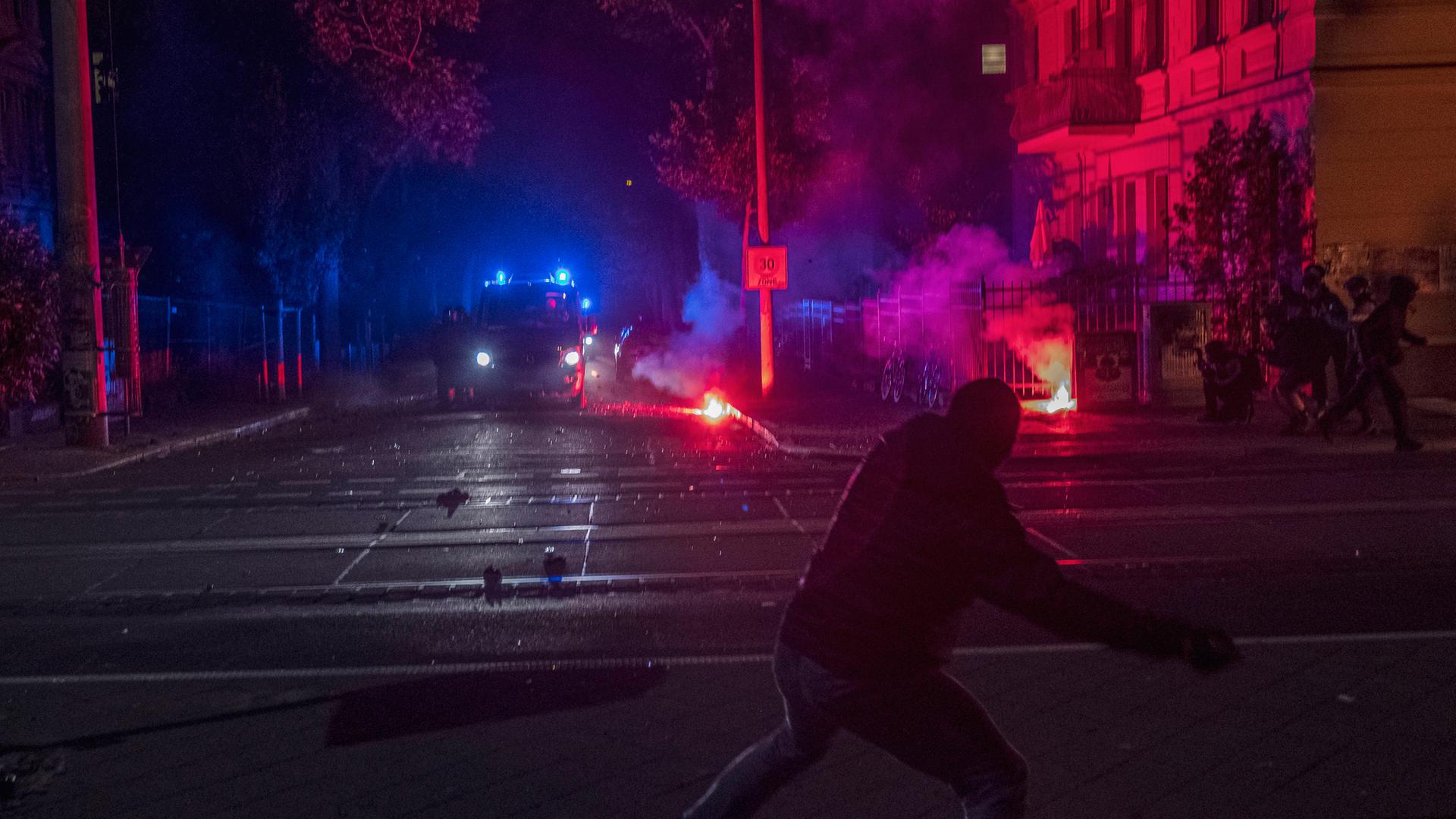 Sachsen, Leipzig: Ein maskerter Demonstrant schmeißt einen Gegenstand in Richtung eines Polizeiwagens.
