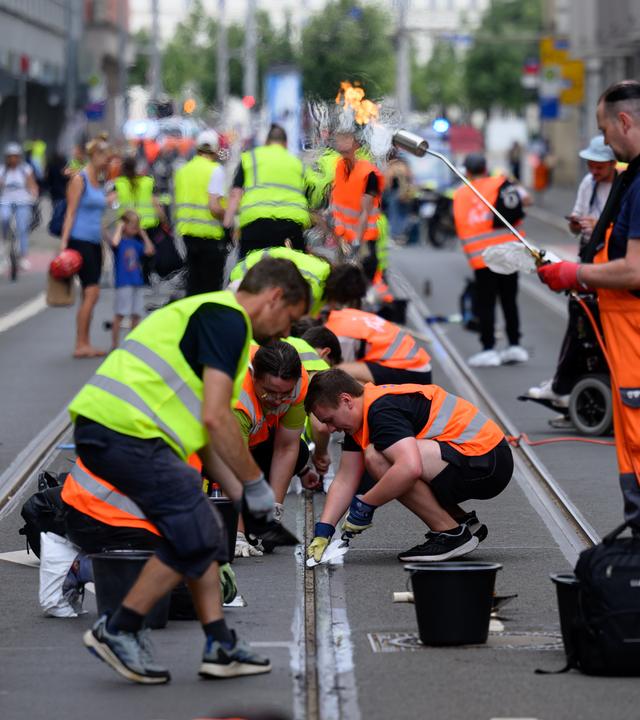 Freiwillige Helferinnen und Helfer befreien im Zentrum Straßenbahnschienen von verklebter Fugenmasse. 