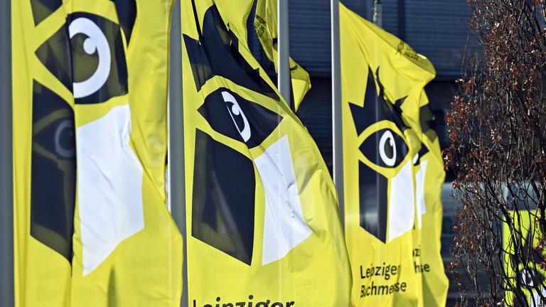 Gelbe Fahnen mit einem stilisierten schwarzen Auge über einem Buch  flattern im Wind.