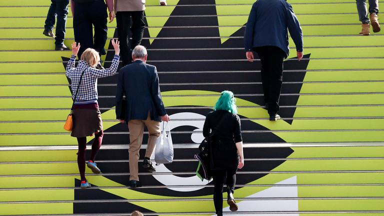 Menschen laufen über eine Treppe mit Logo der Leipziger Buchmesse 2026