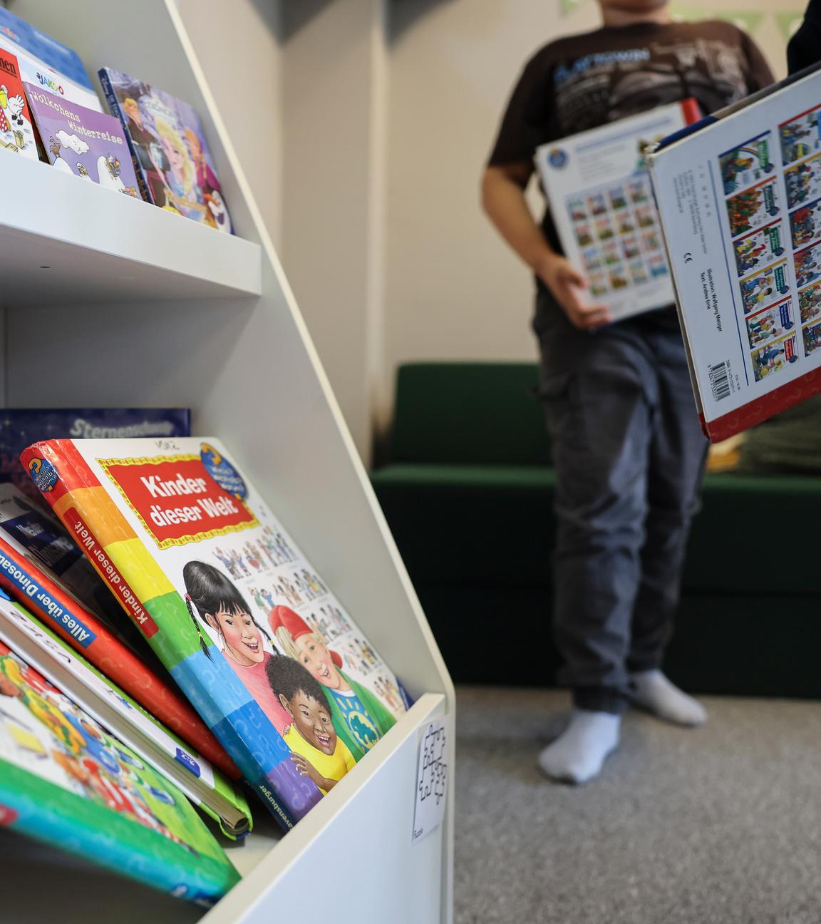 Links ist ein Regal mit Lernbüchern. Rechts stehen zwei Kinder mit Büchern in der Hand.