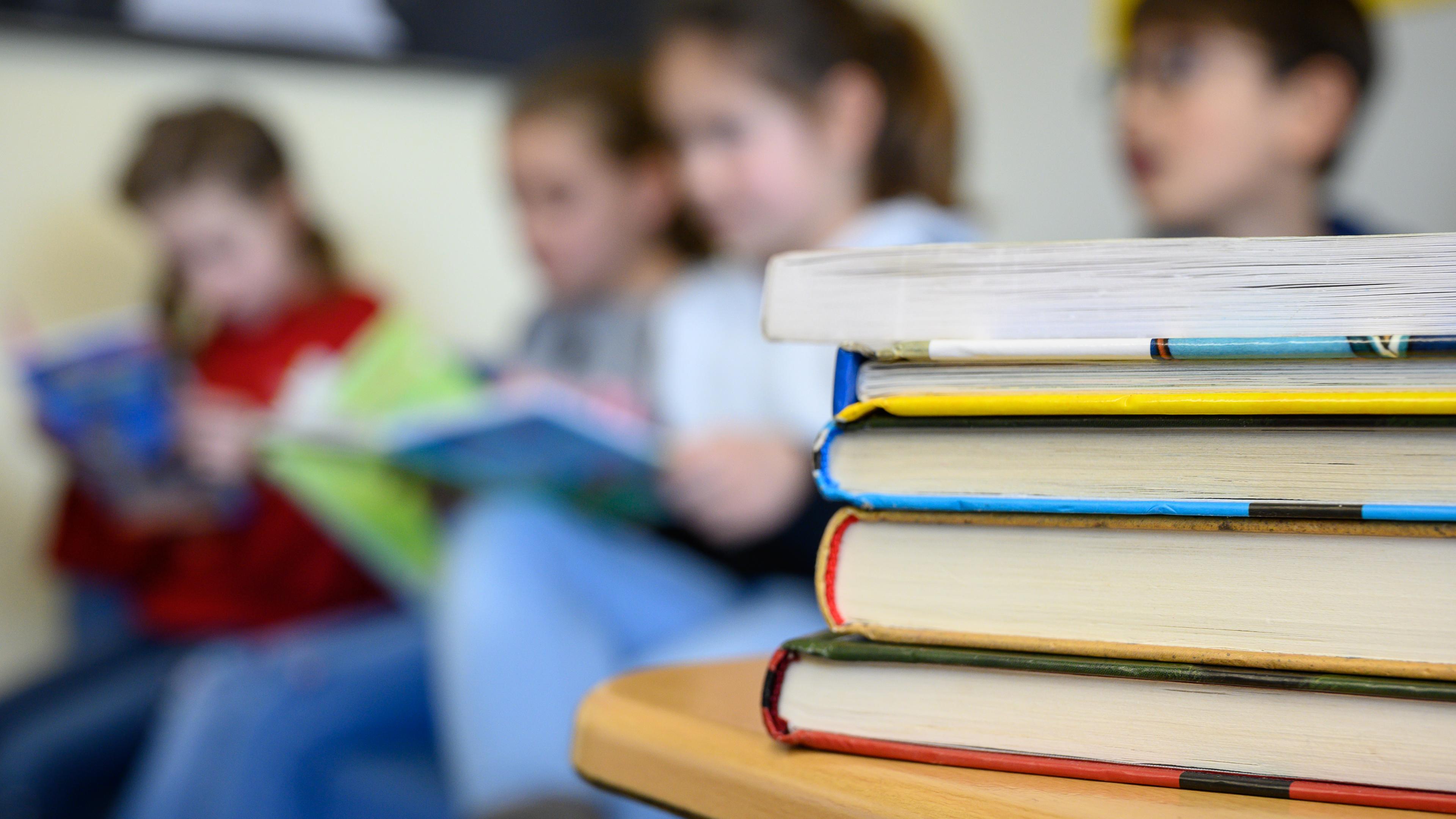 Kinder lesen in einer Grundschule. Die Bücher im Vordergrund sind im Fokus, während die Kinder im Hintergrund unscharf sind.