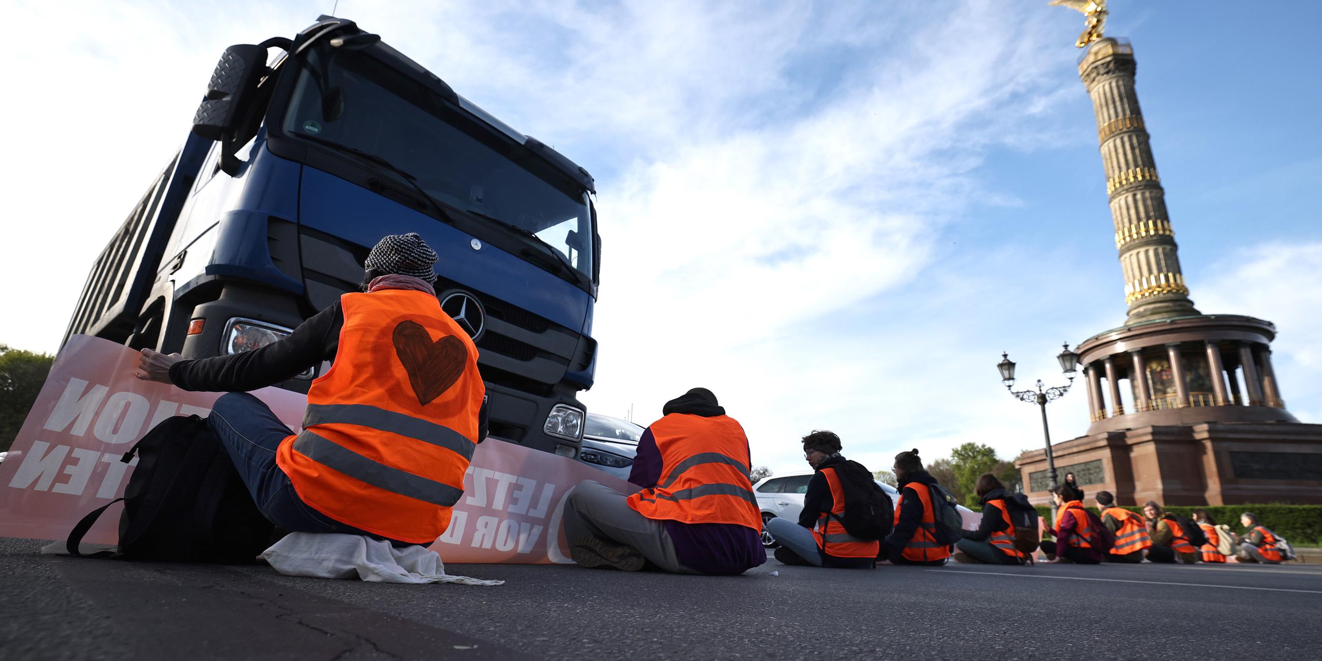 Aktivisten der Letzten Generation sitzen auf der Fahrbahn an der Siegessäule in Berlin und blockieren den Verkehr
