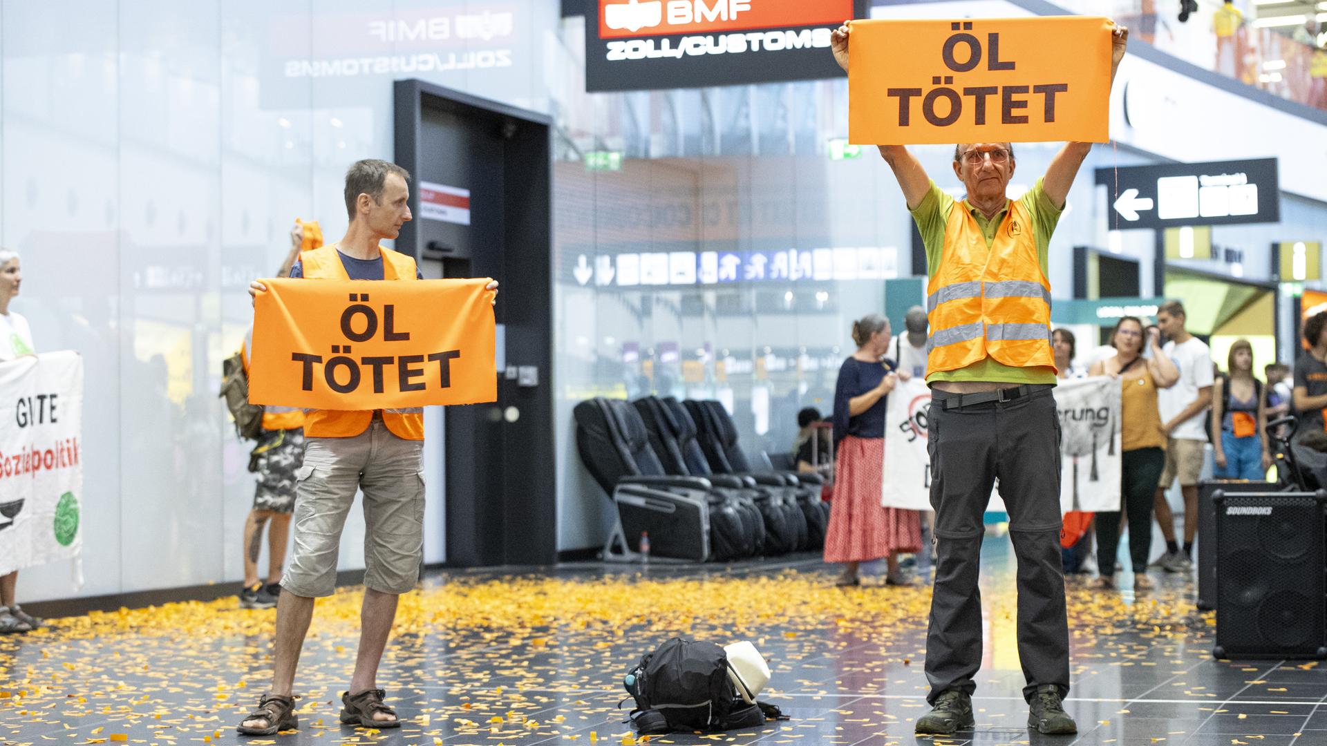 Aktivisten der «Letzten Generation» halten Plakate während einer Störaktion am Flughafen in Wien.