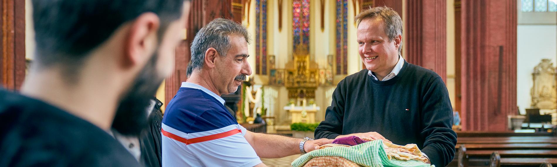 Pfarrer übergibt Decken und Bettwäsche an mehrere Geflüchtete in Kirche.