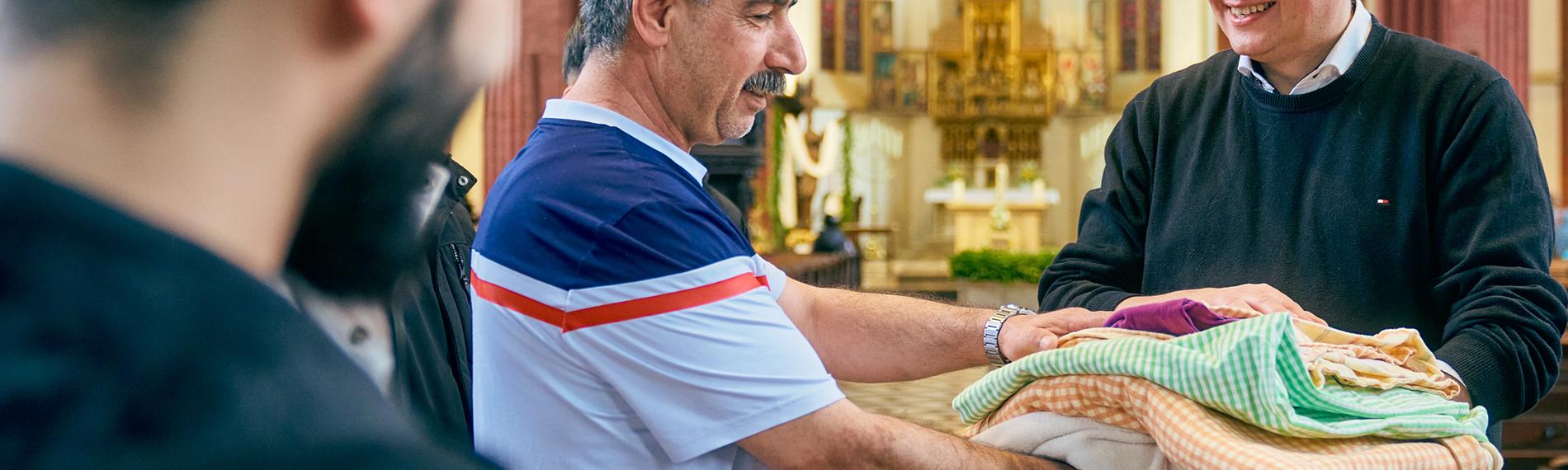 Pfarrer übergibt Decken und Bettwäsche an mehrere Geflüchtete in Kirche.