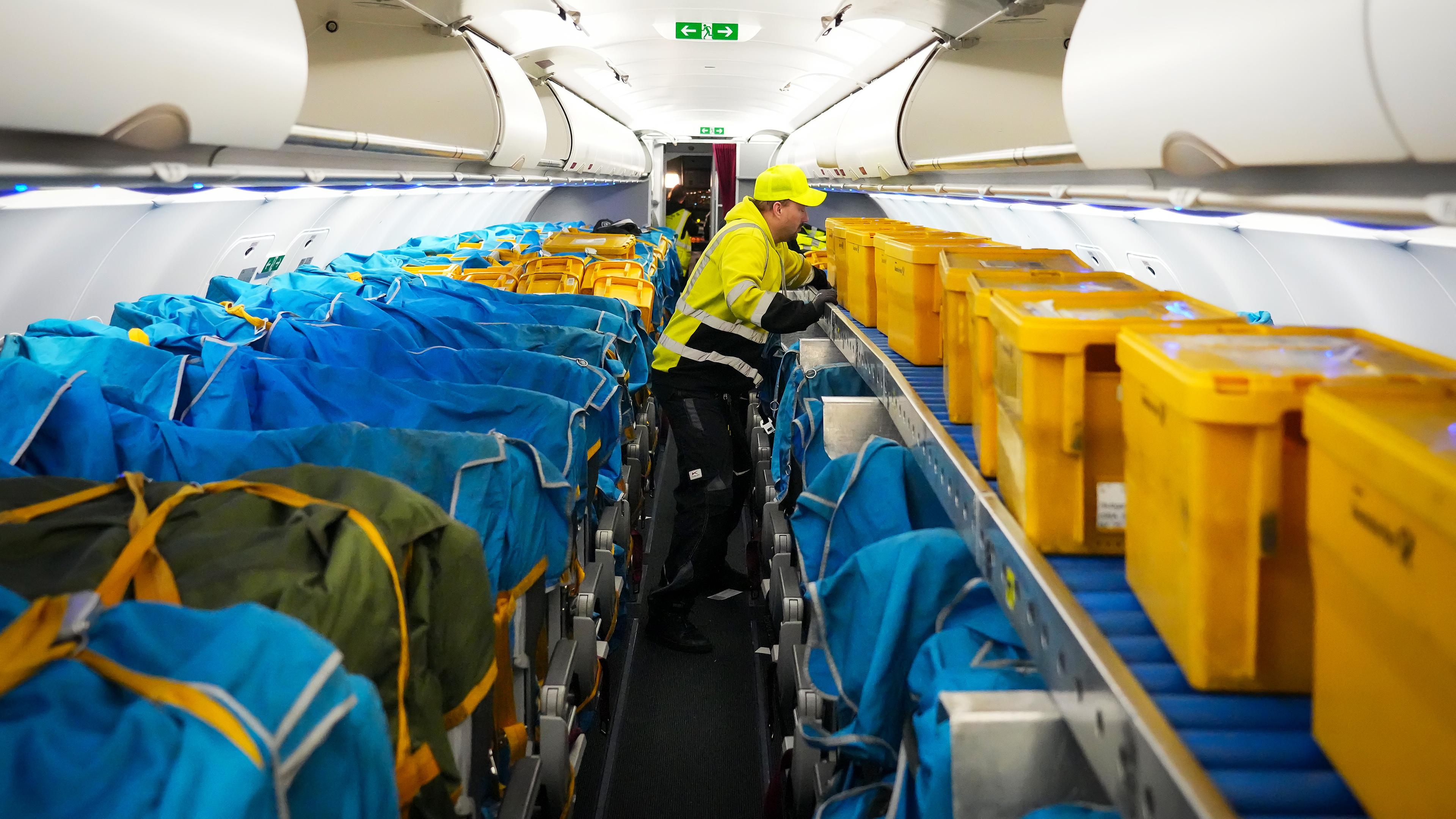  Ein Mitarbeiter der WISAG schiebt in einem Airbus A320-214 auf dem Flughafen Berlin Brandenburg (BER) gelbe Plastikboxen voller Briefe und anderer Post in den vorderen Teil der Kabine. 