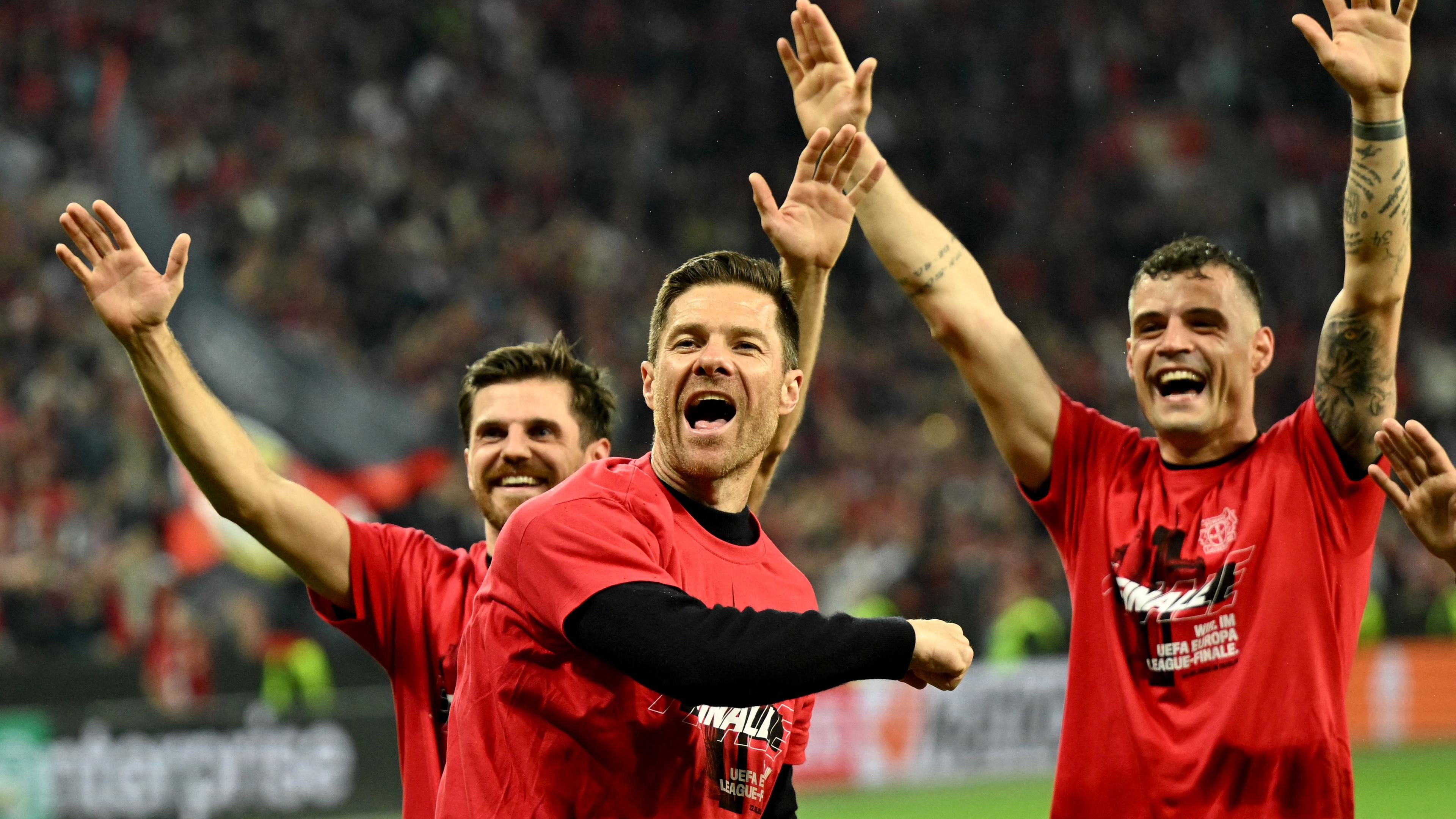 Drei Männer freuen sich auf einem Fußballplatz über den Einzug in Europa-League-Finale. Sie reißen die Arme in den Himmel.