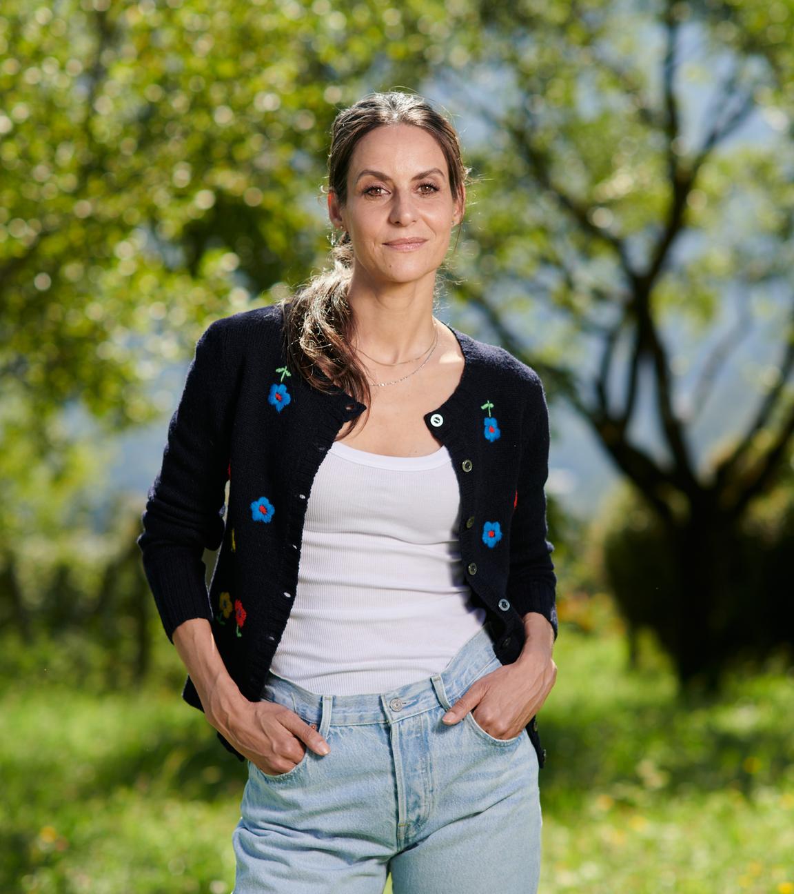 Die junge Schauspielerin Liane Forestieri steht selbstbewusst in Alltagskleidung mit Blick in die Kamera vor einem Hintergrund aus Bäumen und Natur.
