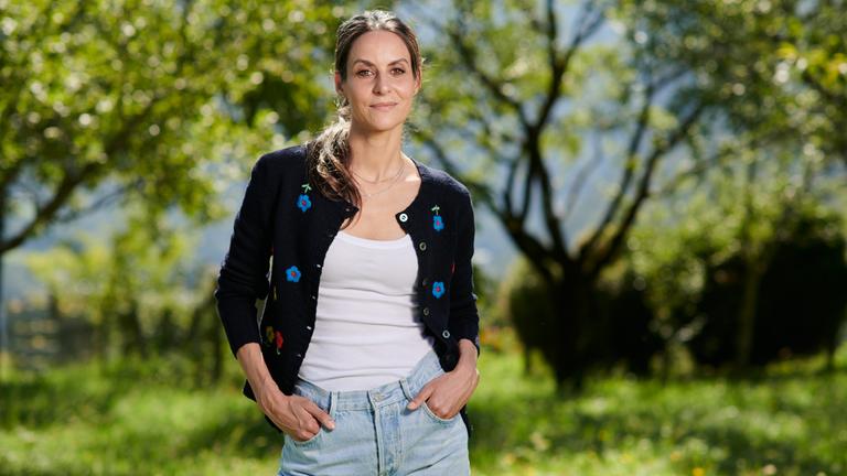 Die junge Schauspielerin Liane Forestieri steht selbstbewusst in Alltagskleidung mit Blick in die Kamera vor einem Hintergrund aus Bäumen und Natur.