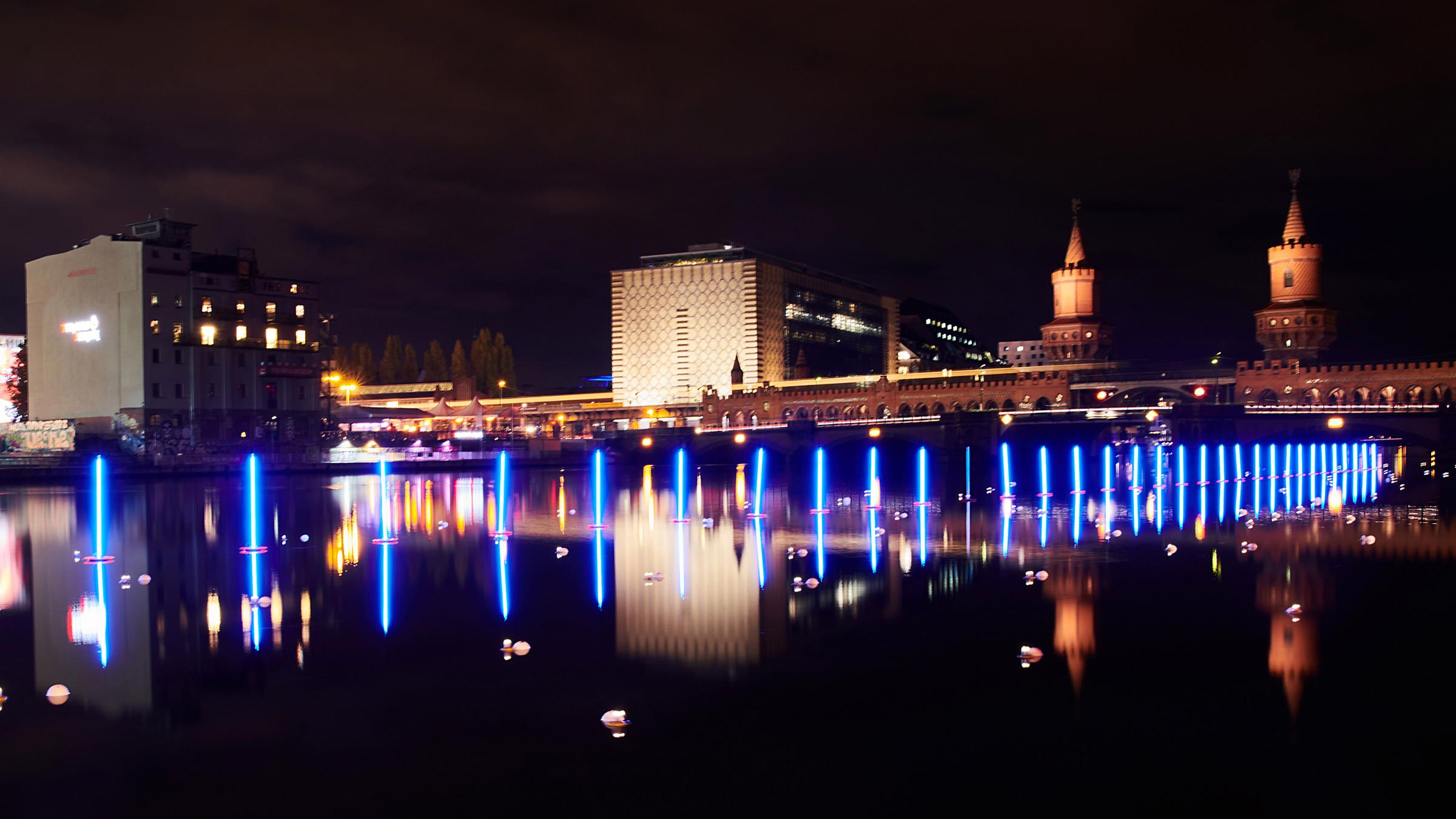 Lichtinstallation von Neonblau leuchtende Stabbojen schwimmen auf der Spree an der Oberbaumbrücke in Berlin am 04.11.2019