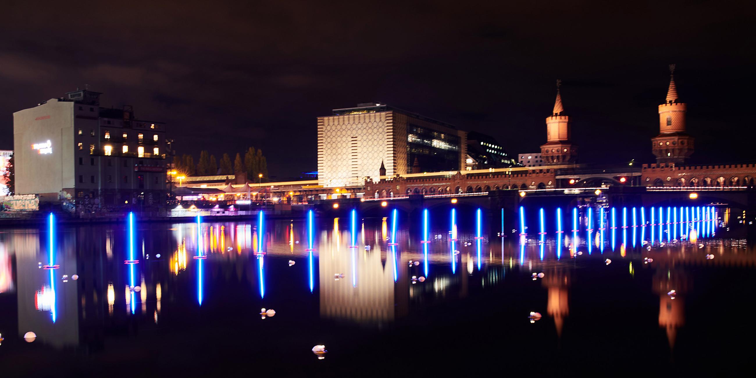 Lichtinstallation von Neonblau leuchtende Stabbojen schwimmen auf der Spree an der Oberbaumbrücke in Berlin am 04.11.2019