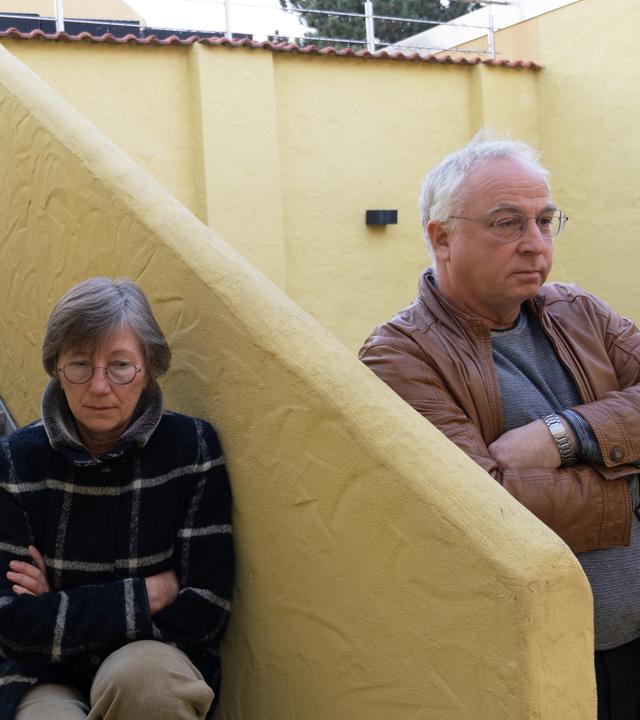 Sylvia sitzt auf einer Treppe, an die sich Jürn anlehnt.