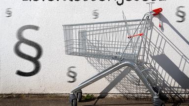 Leerer Einkaufswagen an einer Wand mit Aufschrift: Lieferkettengesetz.