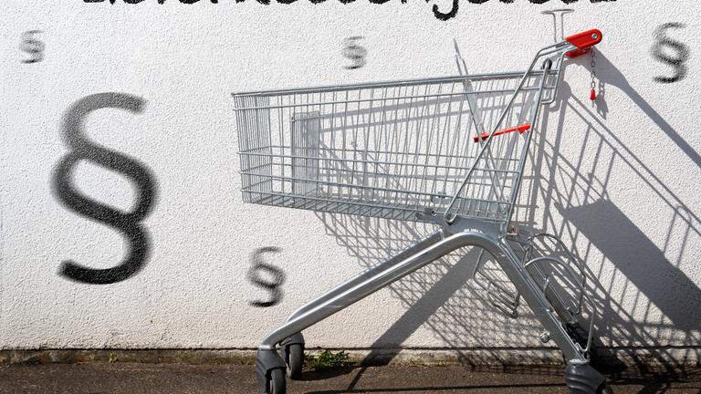 Leerer Einkaufswagen an einer Wand mit Aufschrift: Lieferkettengesetz.
