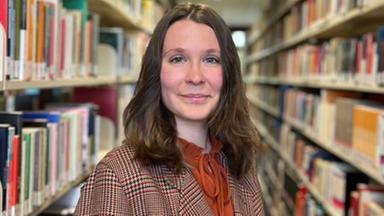 Liliane Kozik steht in einem Gang zwischen zwei Bücherregalen.