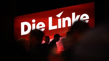 Delegierte sitzen auf dem Bundesparteitag unter dem Logo der Partei Die Linke.