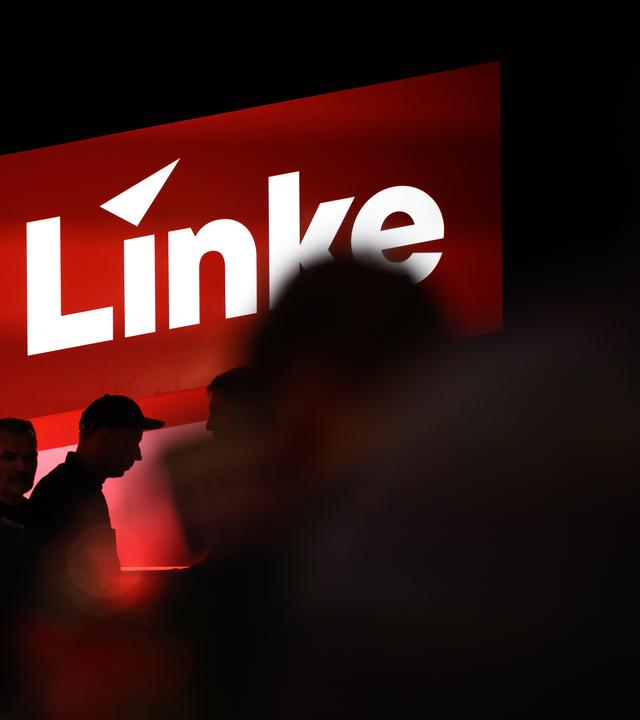Delegierte sitzen auf dem Bundesparteitag unter dem Logo der Partei Die Linke.