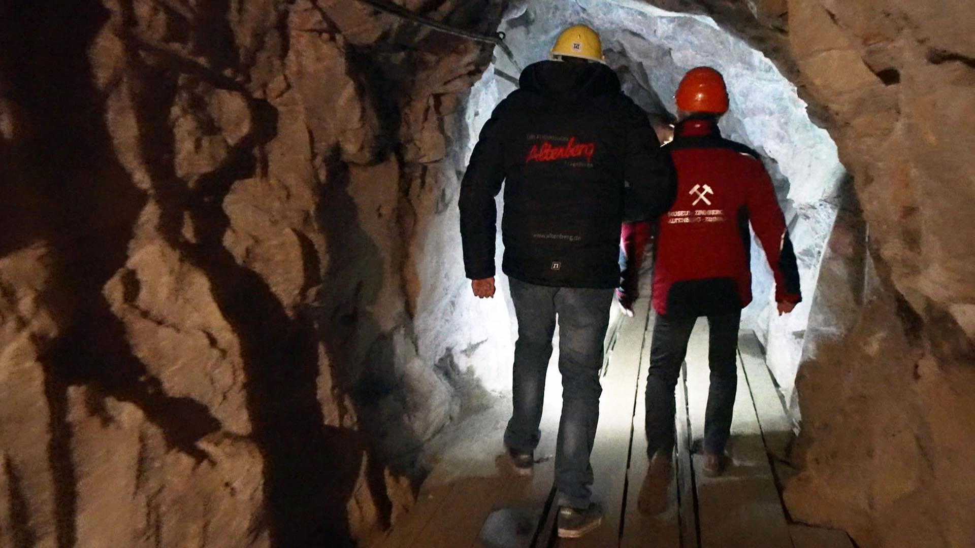 Zwei Männer mit Schutzhelm (Rückansicht) laufen durch einen Bergbautunnel