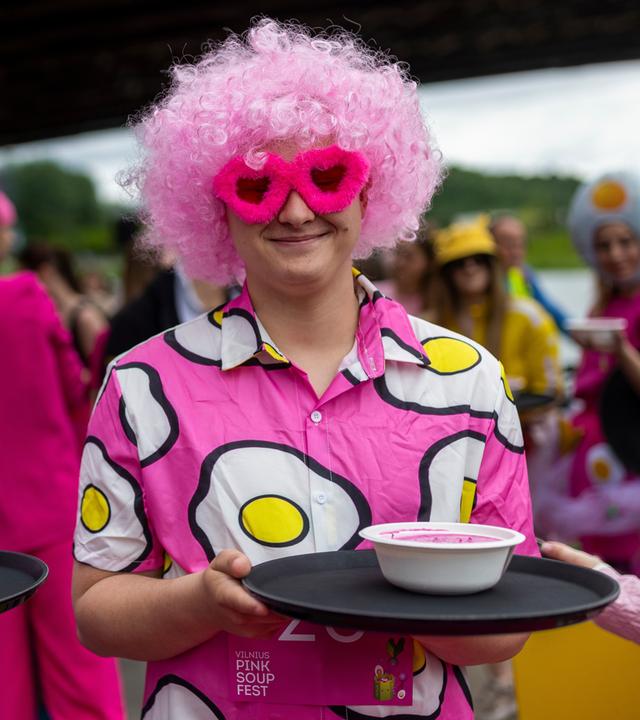 Restaurantkellner in amüsanten und festlichen Kostümen bereiten sich darauf vor, beim „Pink Soup Fest“ in Vilnius (Litauen) am Laufwettbewerb mit Schalen voller rosa Suppe teilzunehmen.