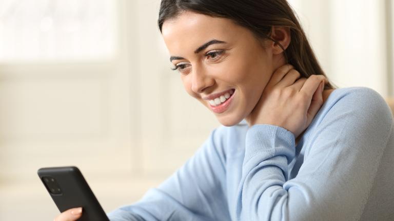 Eine Frau sitzt am Tisch und benutzt ihr Smartphone.