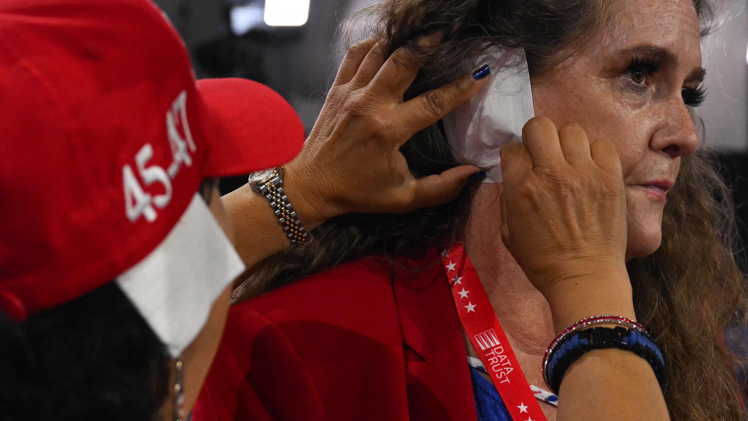 Stacey Goodman aus Arizona hilft Liz Harris aus Solidarität mit Donald Trump, während des dritten Tages der Republican National Convention 2024 im Fiserv Forum in Milwaukee, am 17.07.2024 ein Pflaster über ihr Ohr zu kleben.