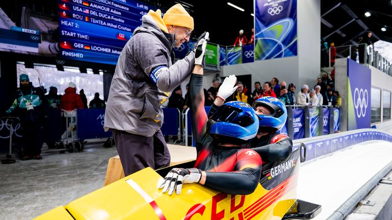 Die deutsche Bobsportler Johannes Lochner und Georg Fleischhauer klatschen nach ihrem Lauf bei den Olympischen Winterspielen 2026 in Cortina ihren Trainer ab