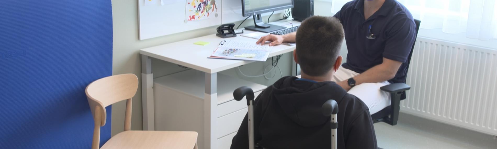 Junge im Rollstuhl spricht mit Kinderarzt