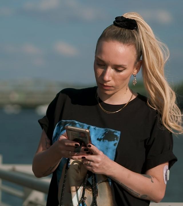 Long Covid: Visa Vie, bürgerlich Charlotte Mellahn, Moderatorin auf Brücke stehend und in Handy tippend, Hintergrund Wasser