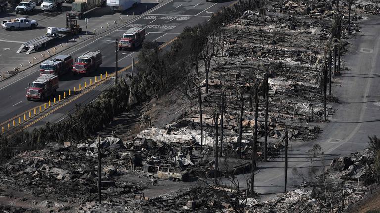 Fahrzeuge der Feuerwehr fahren auf einer Straße neben Brandruinen in der kalifornischen Stadt Los Angeles.