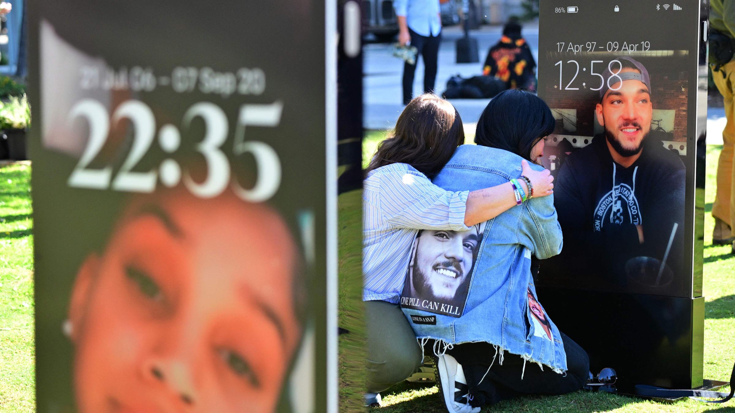 Zwei trauernde Familienmitglieder vor einem großen Handyscreen, auf dem das Foto eines Jugendlichen zu sehen ist.