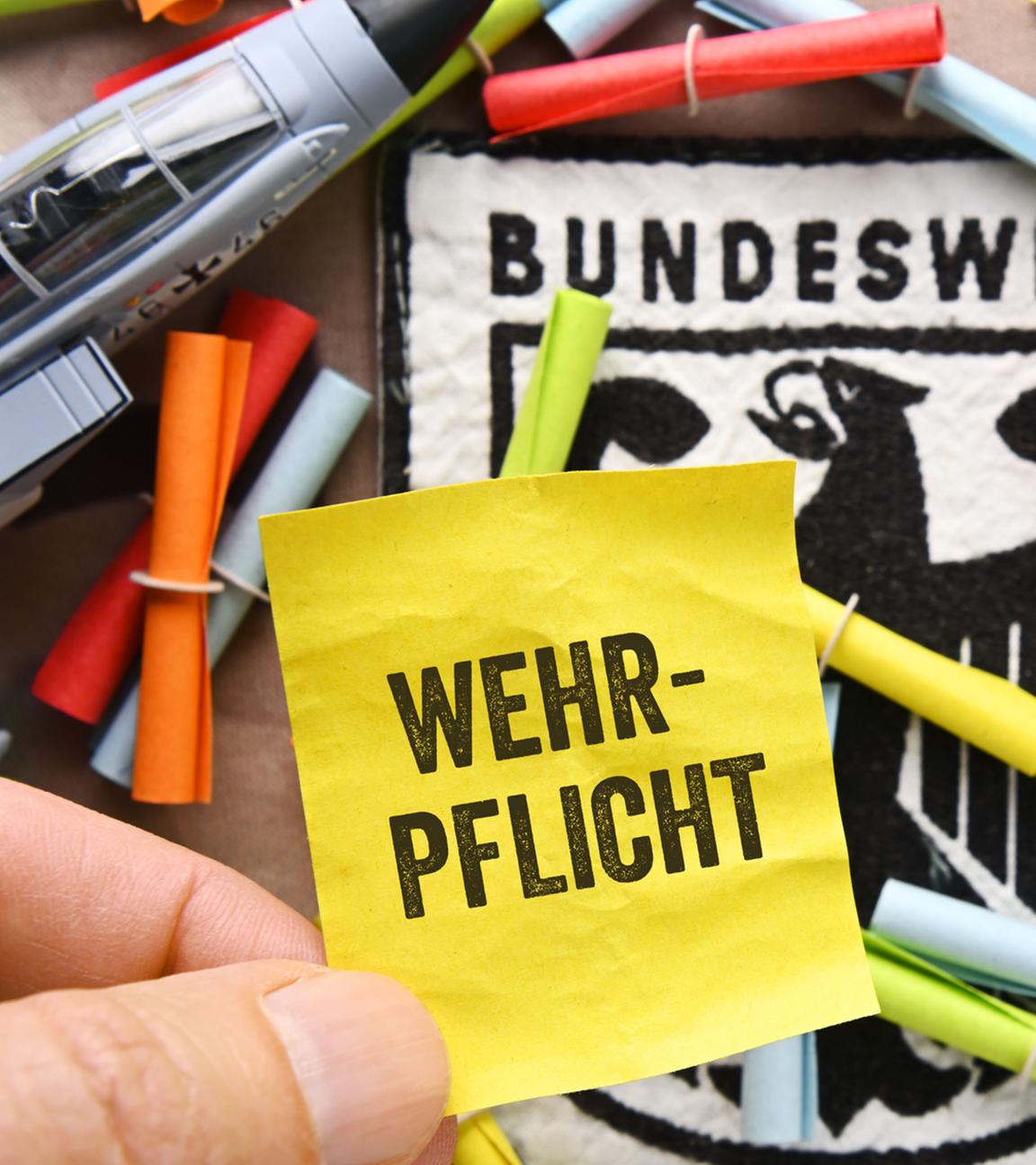 Hand hält Los mit Aufschrift Wehrpflicht vor Bundeswehrabzeichen und Losen