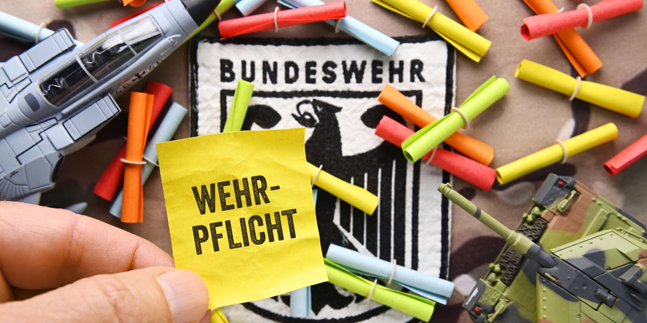 Hand hält Los mit Aufschrift Wehrpflicht vor Bundeswehrabzeichen und Losen