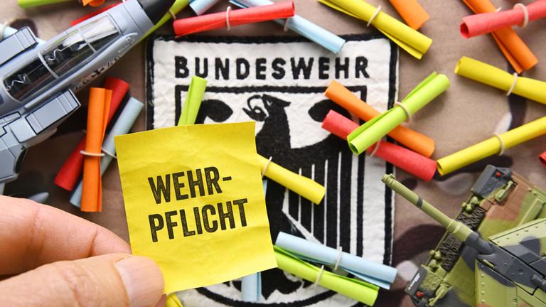 Hand hält Los mit Aufschrift Wehrpflicht vor Bundeswehrabzeichen und Losen