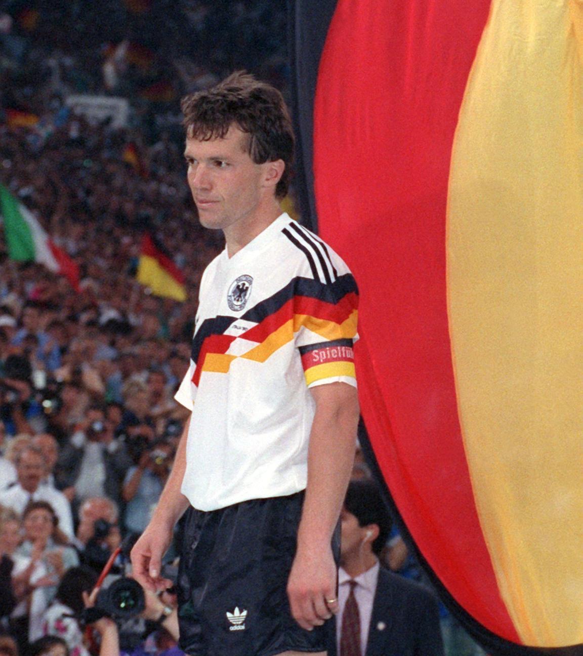 Lothar Matthaeus im Deutschandtrikot vor einer Deutschland-Flagge und erwartet die Siegerehrung 1990.