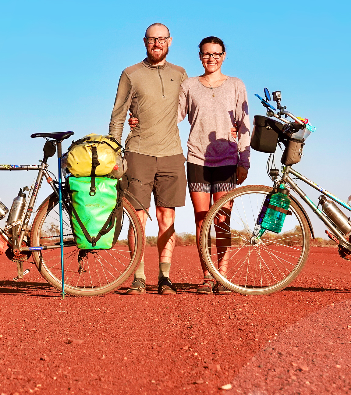 Tobi und Louisa stehen zwischen ihren Fahrrädern in einer kargen Landschaft mit blauem Himmel.