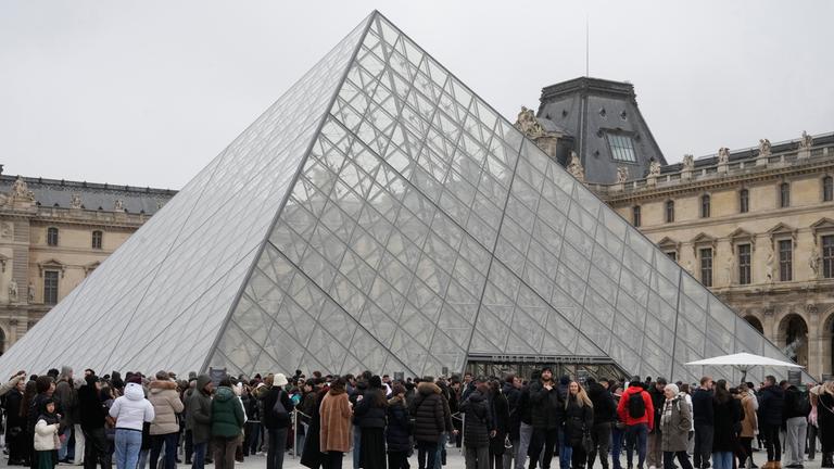 Eine Menschenschlange steht vor dem Louvre-Museum an der gläsernen Pyramide.