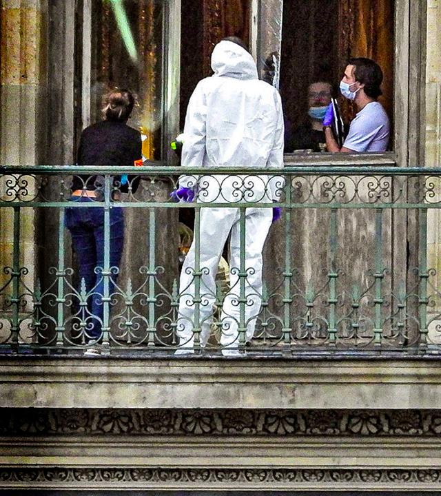 Vier Personen, davon eine im weißen Schutzanzug, stehen nach dem Einbruch in den Louvre auf einem Balkon des Gebäude.
