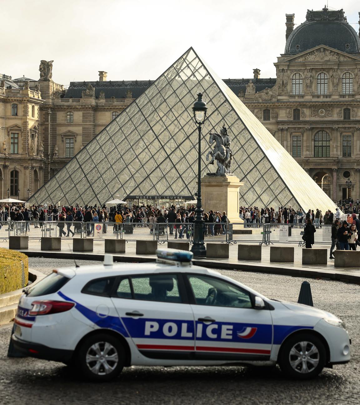  26.10.2025, Frankreich, Paris: Ein Polizeiauto parkt im Hof des Louvre während Besucher vor der Glaspyramide in einer Schlange stehen. 