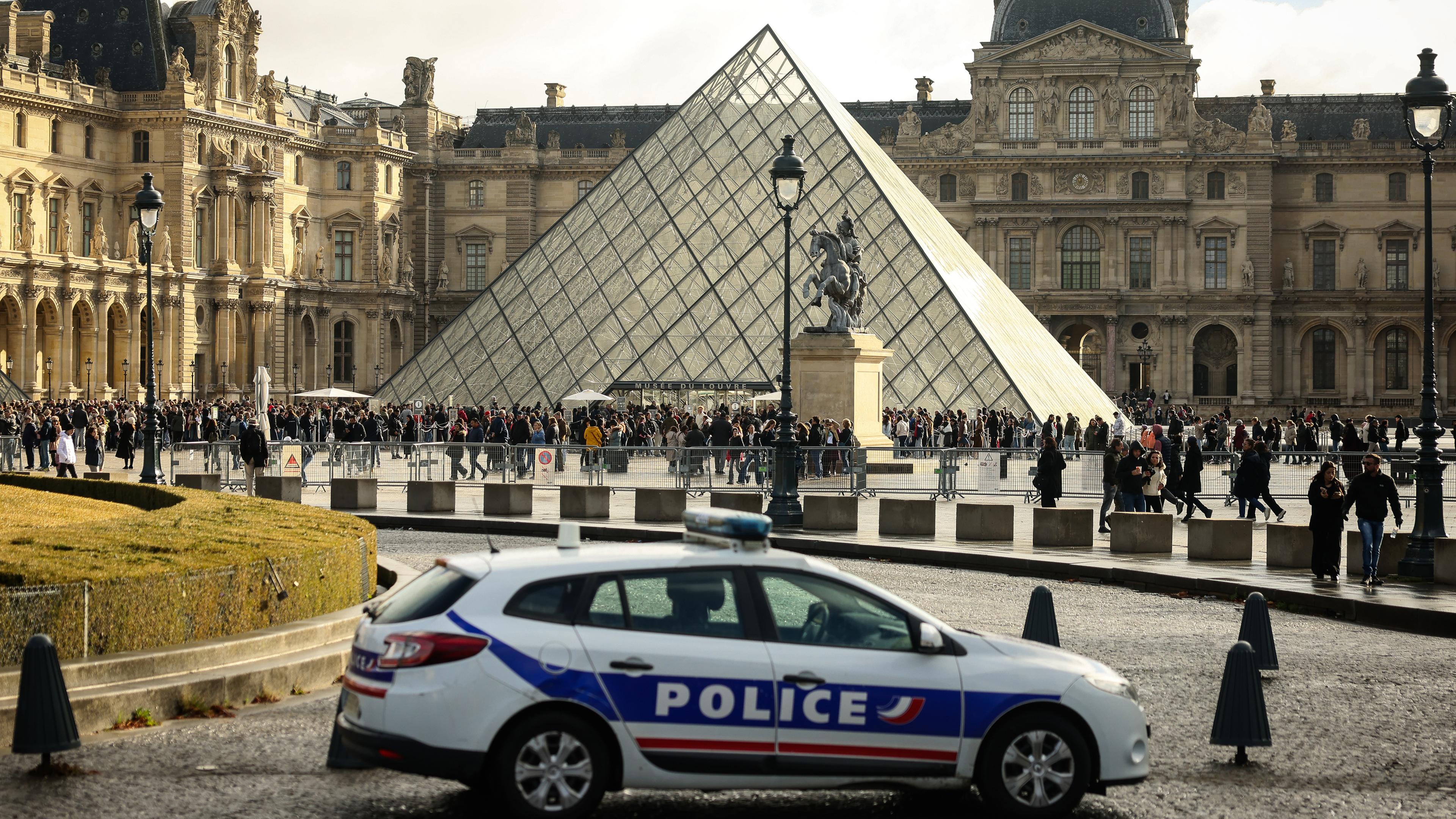 26.10.2025, Frankreich, Paris: Ein Polizeiauto parkt im Hof des Louvre während Besucher vor der Glaspyramide in einer Schlange stehen. 