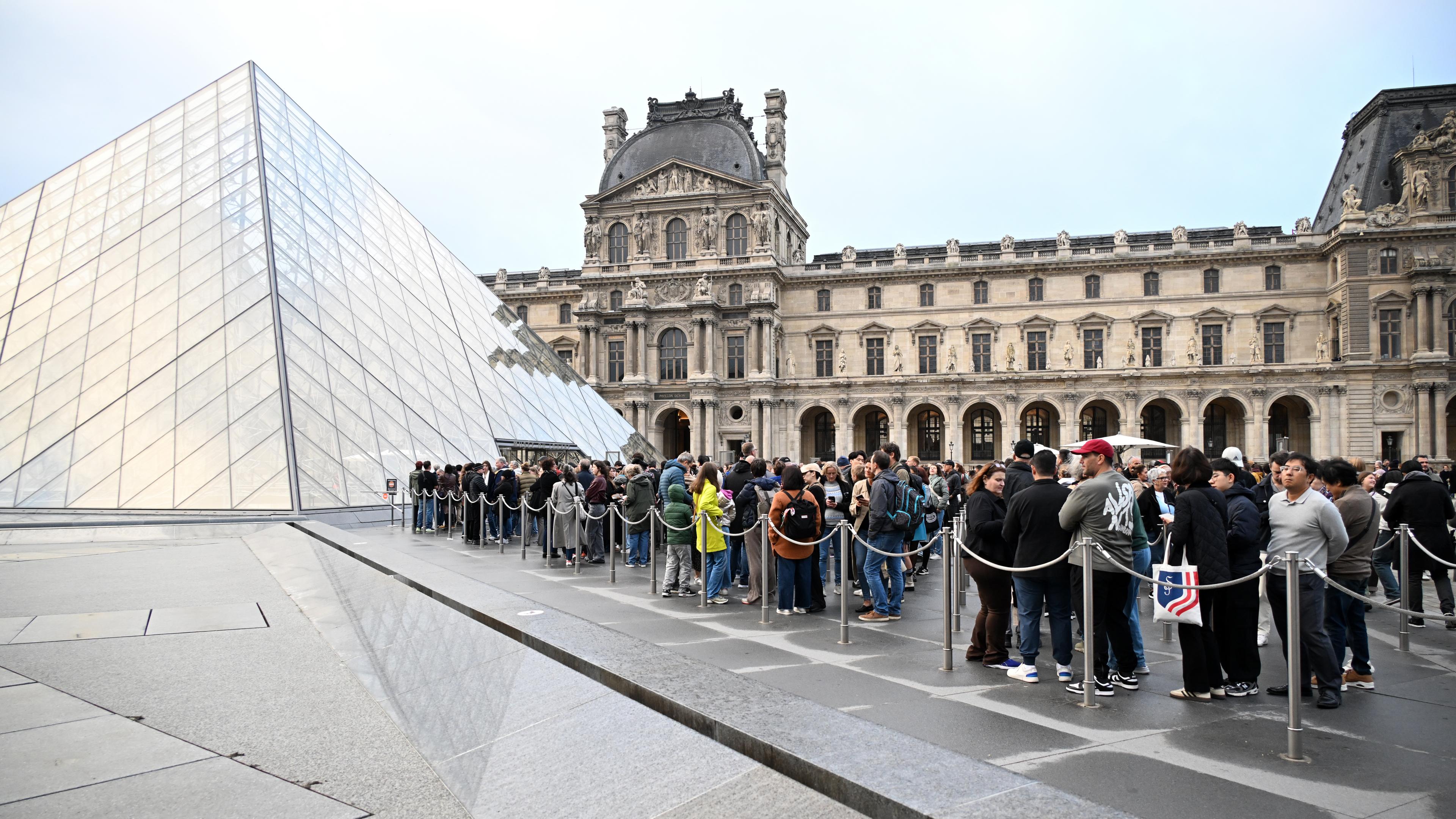 In Paris stehen Menschen im Hof der Louvre-Pyramide Schlange.