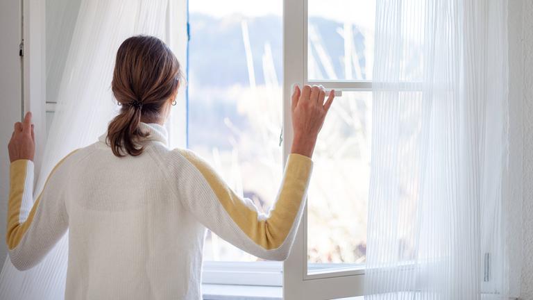 Eine Frau ist von hinten an einem weit geöffneten Fenster zu sehen.