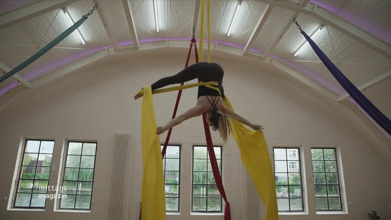 Frau zeigt eine Figut in der Luft und hängt in zwei Seilen