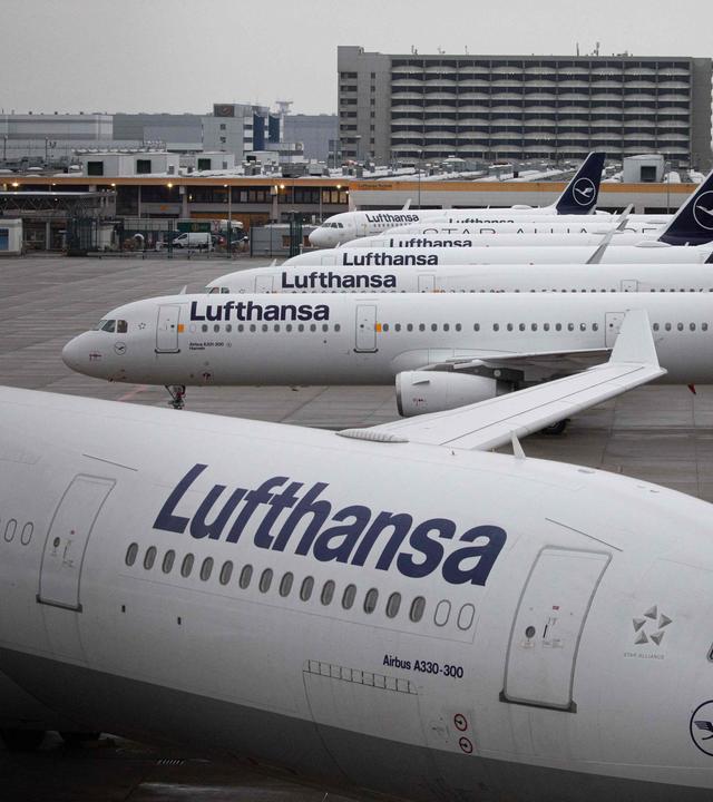 mehrere Lufthansa-Flugzeuge, im Hintergrund ein grauer Himmel 