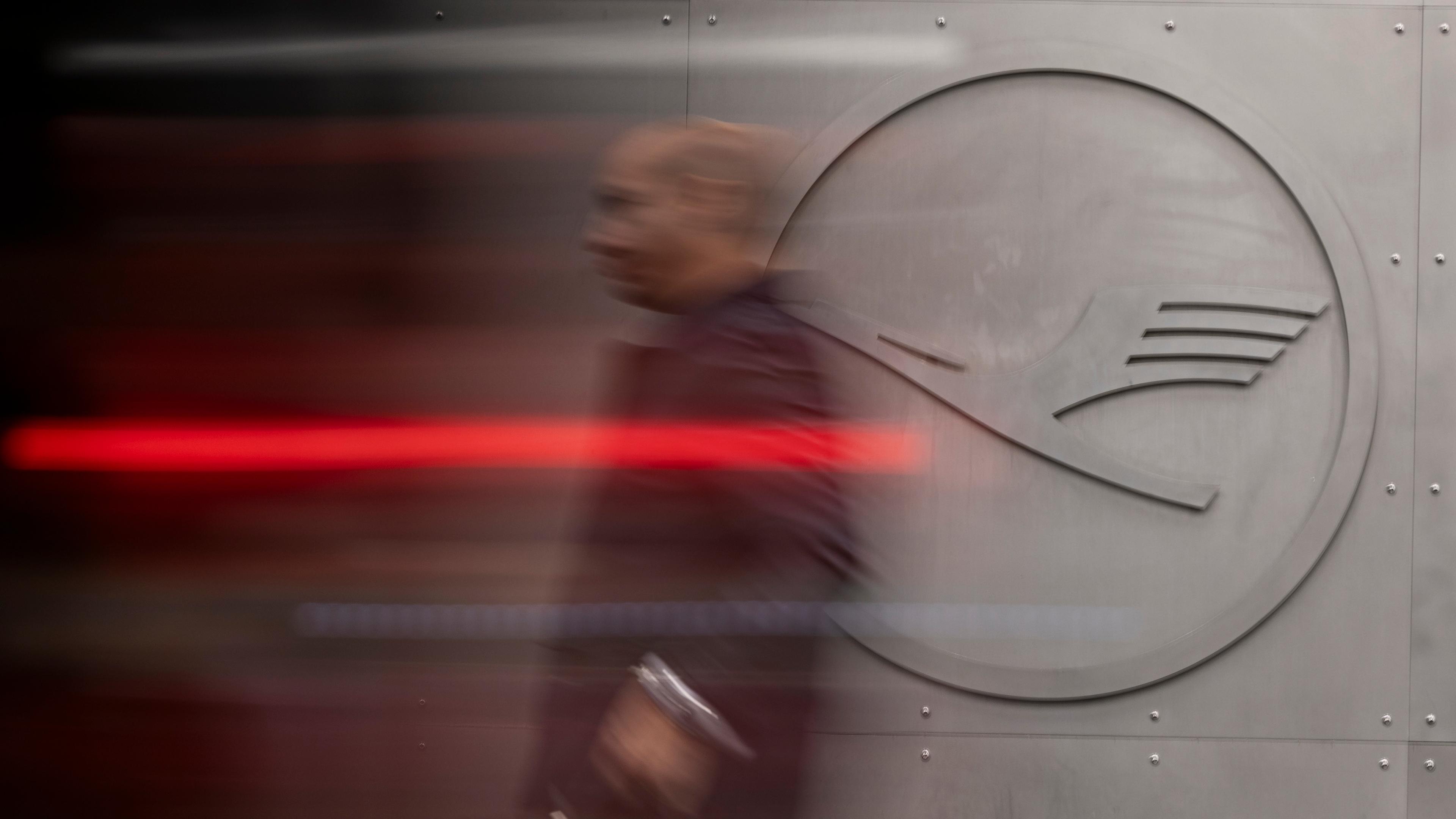 Ein Mann geht vor einem Lufthansa-Logo am Frankfurter Flughafen. 