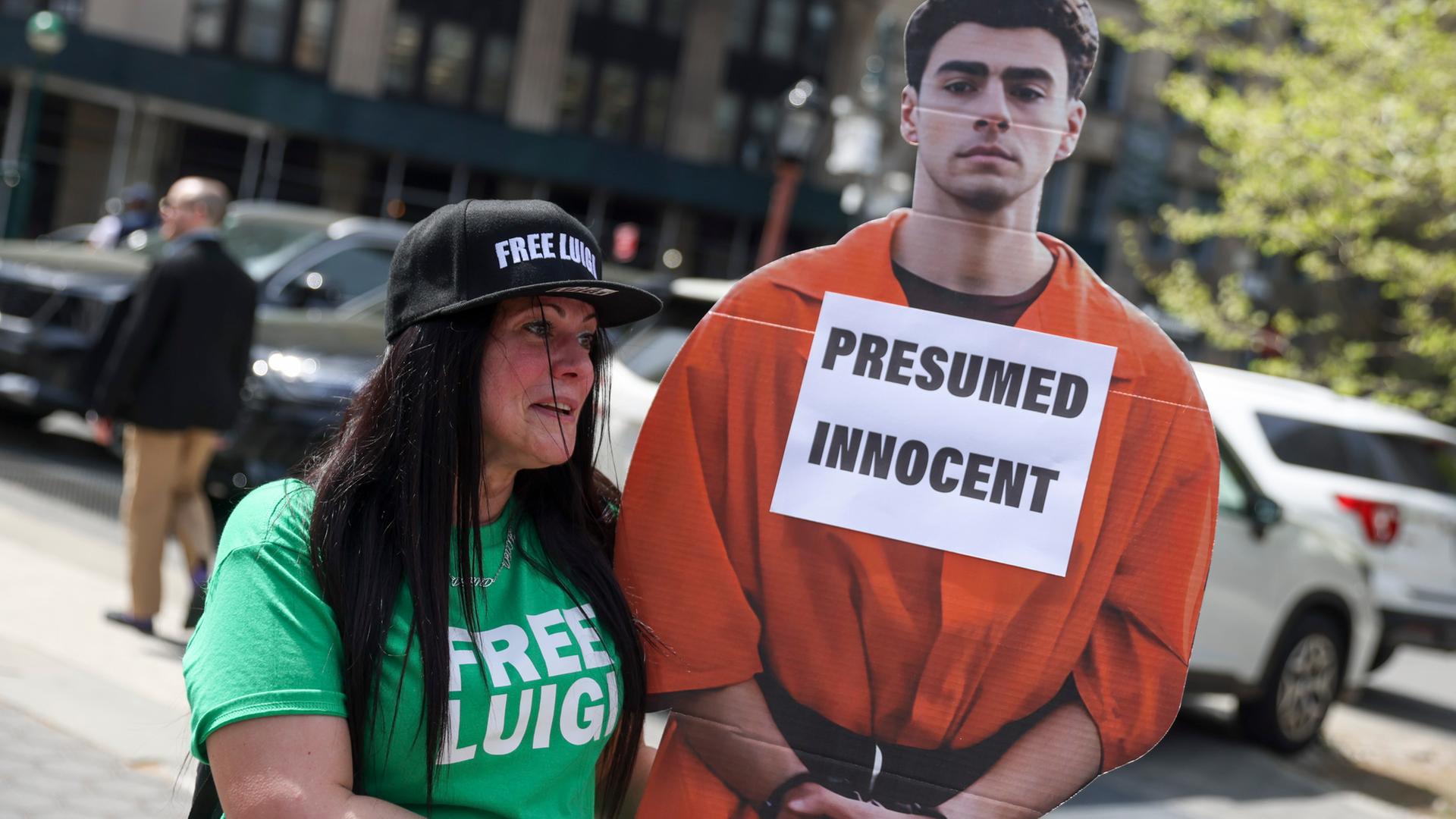 Eine Protestierende mit einem Pappaufsteller von Luigi Mangione, Aufschrift "Presumed innocent"/"mutmaßlich unschuldig"