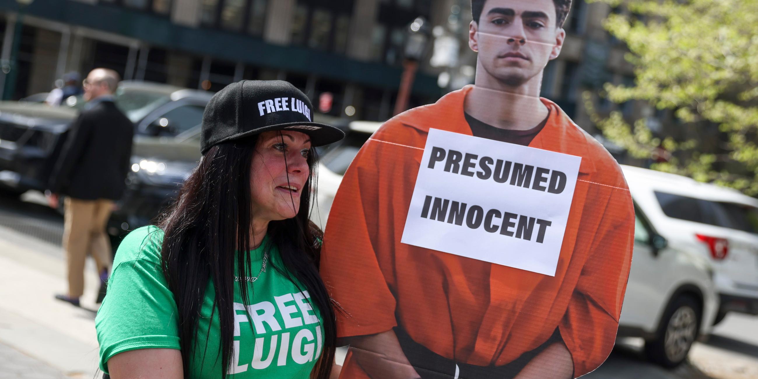 Eine Protestierende mit einem Pappaufsteller von Luigi Mangione, Aufschrift "Presumed innocent"/"mutmaßlich unschuldig"
