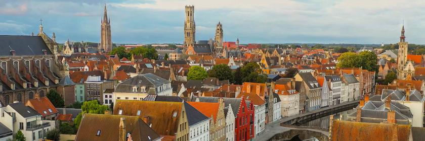 Blick von schräg oben auf Brügge, einer Stadt mit mittelalterlichen Gebäuden, durch die sich ein Kanal zieht.