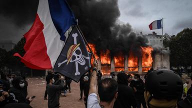 Ein Demonstrant hält eine französische Nationalflagge sowie ein Logo des beliebten japanischen Mangas „One Piece“ – ein Symbol, das weltweit von Protestbewegungen der Generation Z aufgegriffen wurde – vor das Tourismusbüro von Lyon, das während einer Demonstration gegen die „hohen Lebenshaltungskosten“ in Brand gesetzt worden war. Das Ereignis fand am 17. Oktober 2026 in Lyon im Südosten Frankreichs im Rahmen eines landesweiten Mobilisierungsaufrufs statt, der verschiedene Gruppen zusammenbrachte, die ihrem Unmut Ausdruck verliehen: ehemalige „Gelbwesten“, Schüler und Studierende, Klimaaktivisten sowie Landwirte.